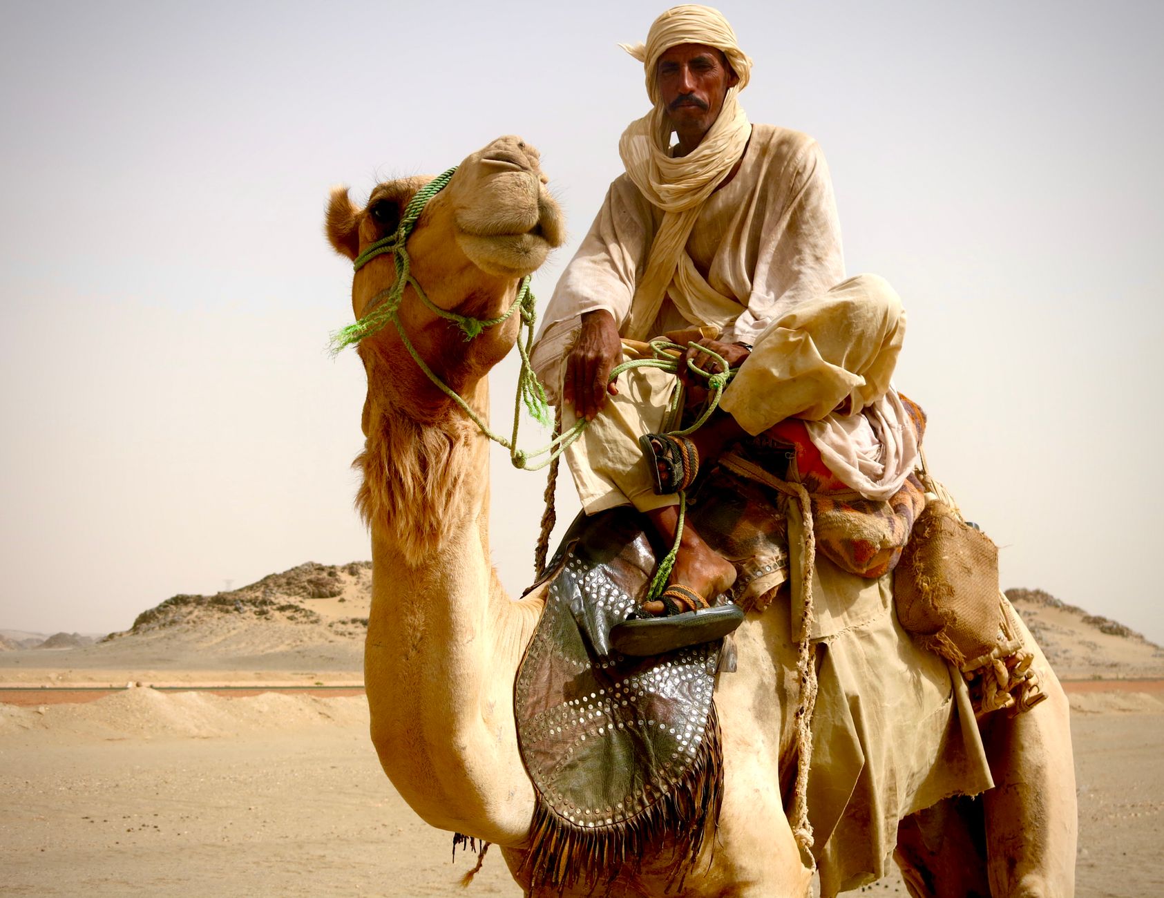 Nomadic pastoralist riding a camel through the arid gravel plains of the eastern Sudanese desert