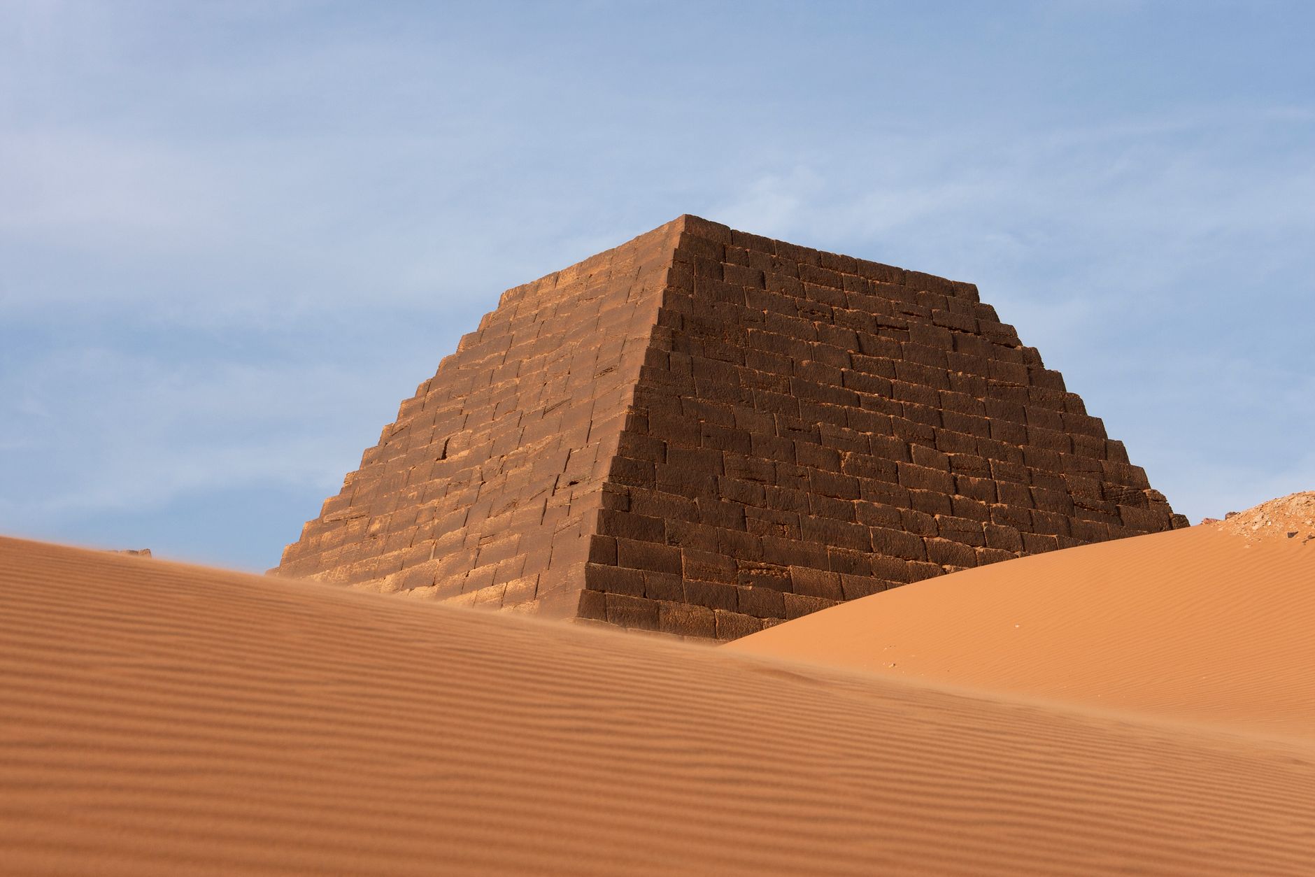 Ancient Nubian funerary pyramid surrounded by wind-rippled desert sand dunes