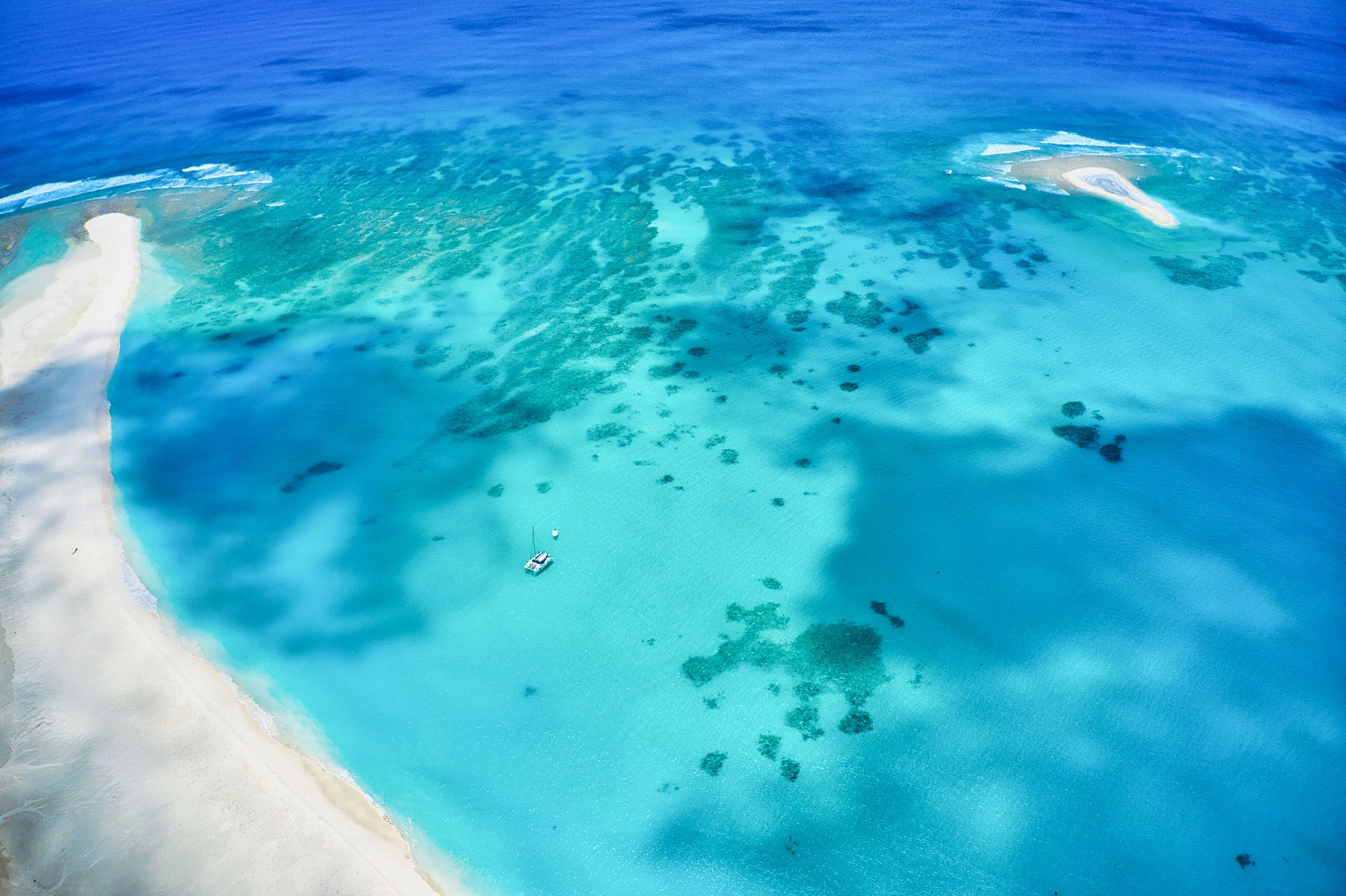 Glass bottom excursion boat anchored in shallow crystalline turquoise water over a sandy reef flat