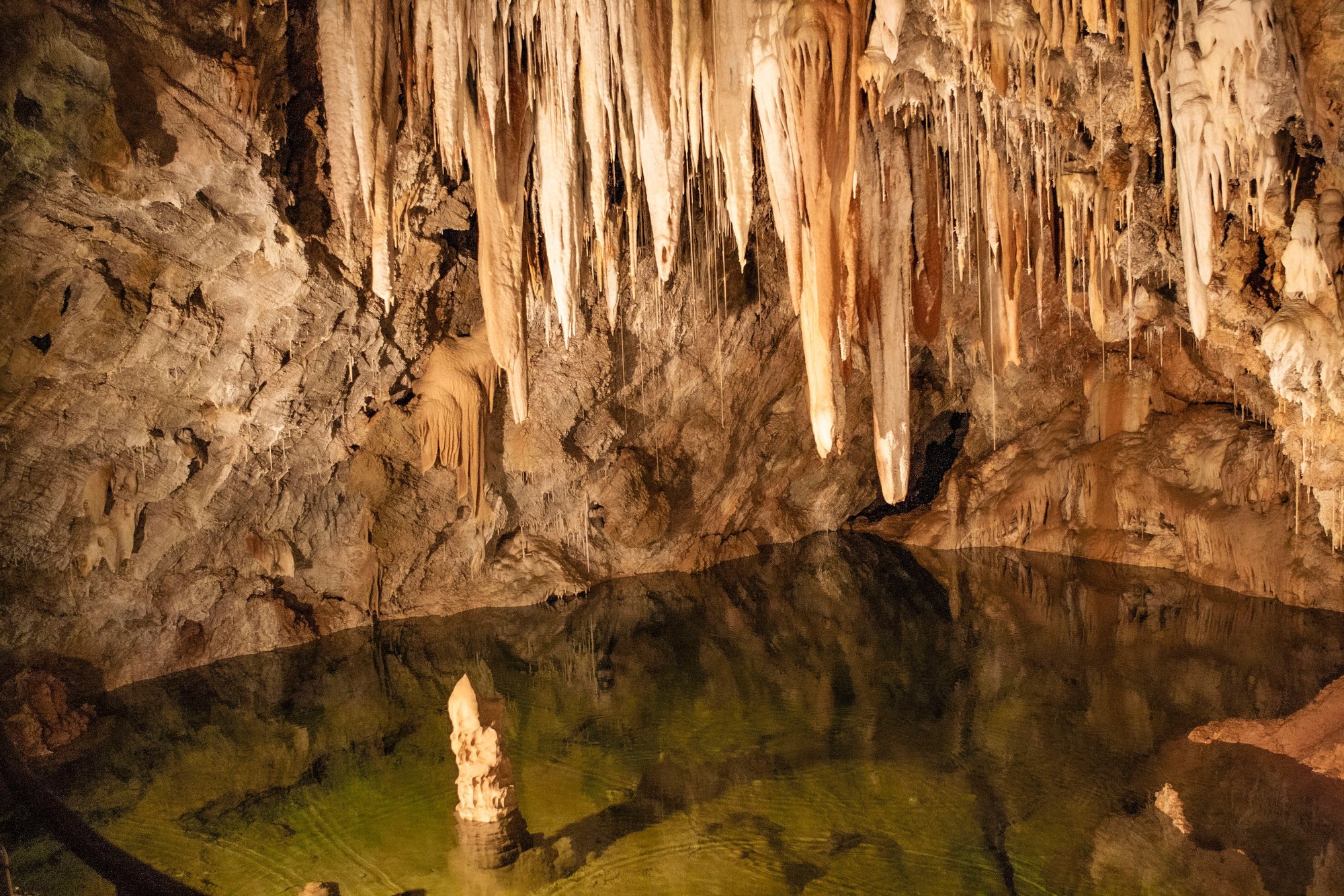 Stalactites and tranquil natural freshwater pool inside a limestone cave