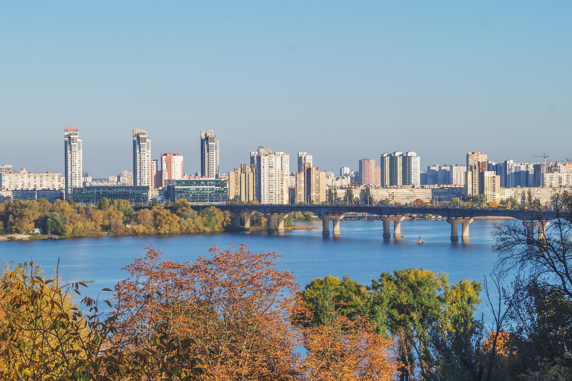 Panorama of Kyiv cityscape and bridges spanning the broad Dnieper River under autumn sunlight