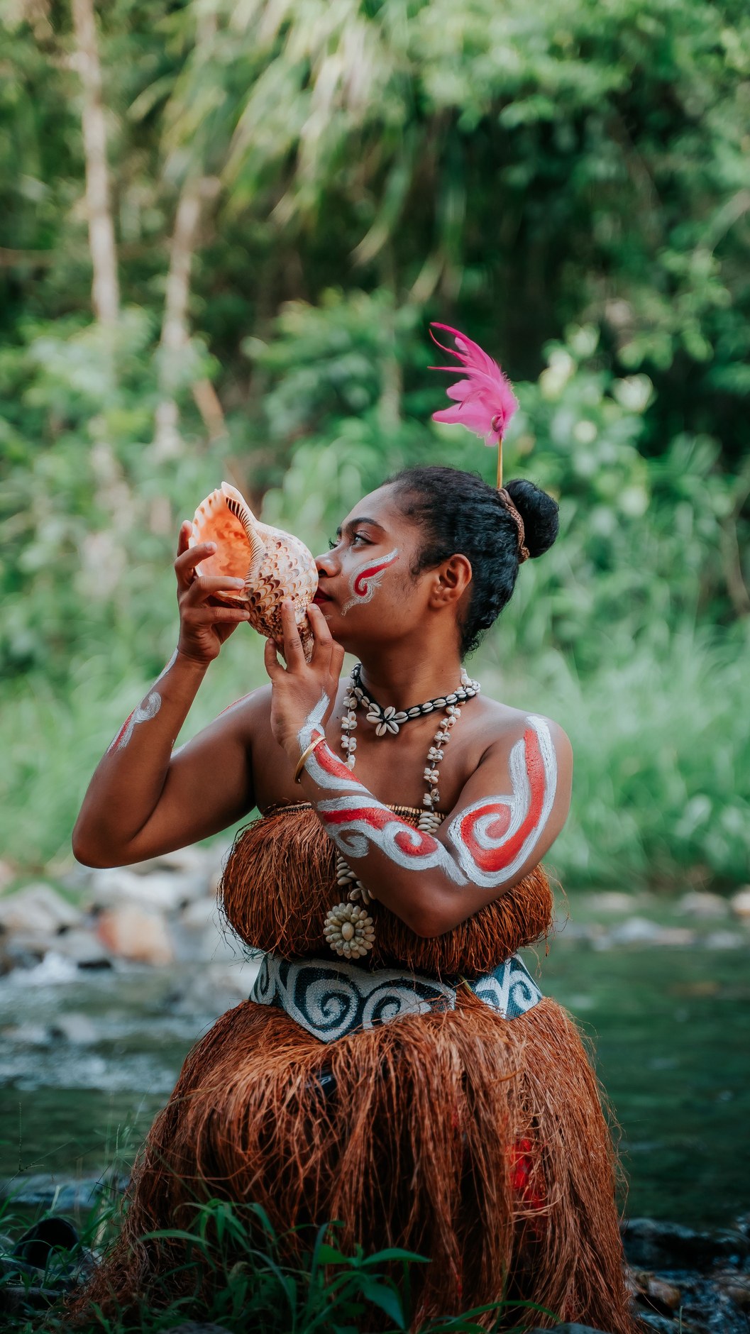 Traditional Melanesian cultural portrait in lush tropical rainforest setting beside clear running water
