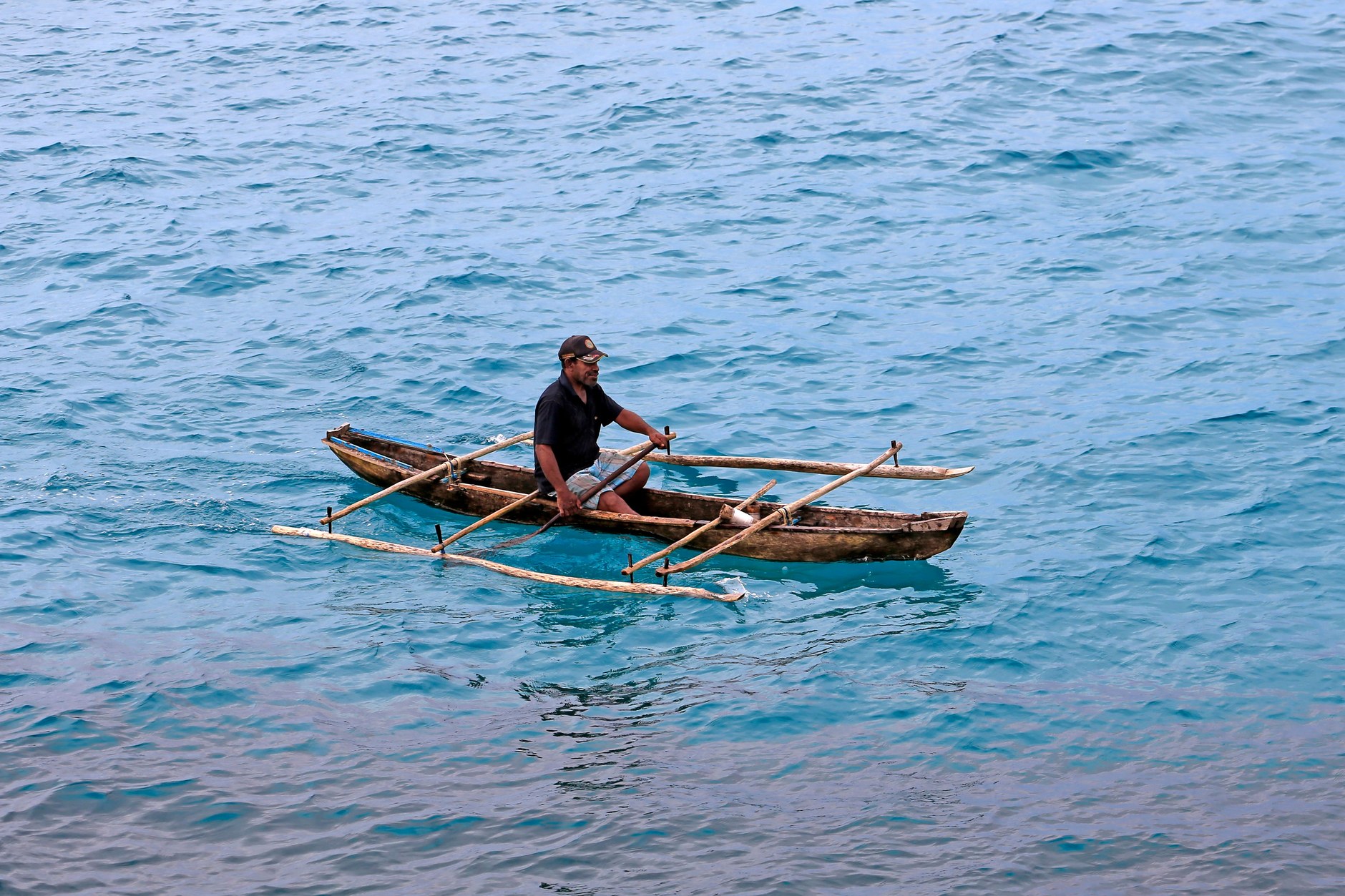 A traditional wooden outrigger dugout canoe navigating crystal-clear turquoise waters in Vanuatu
