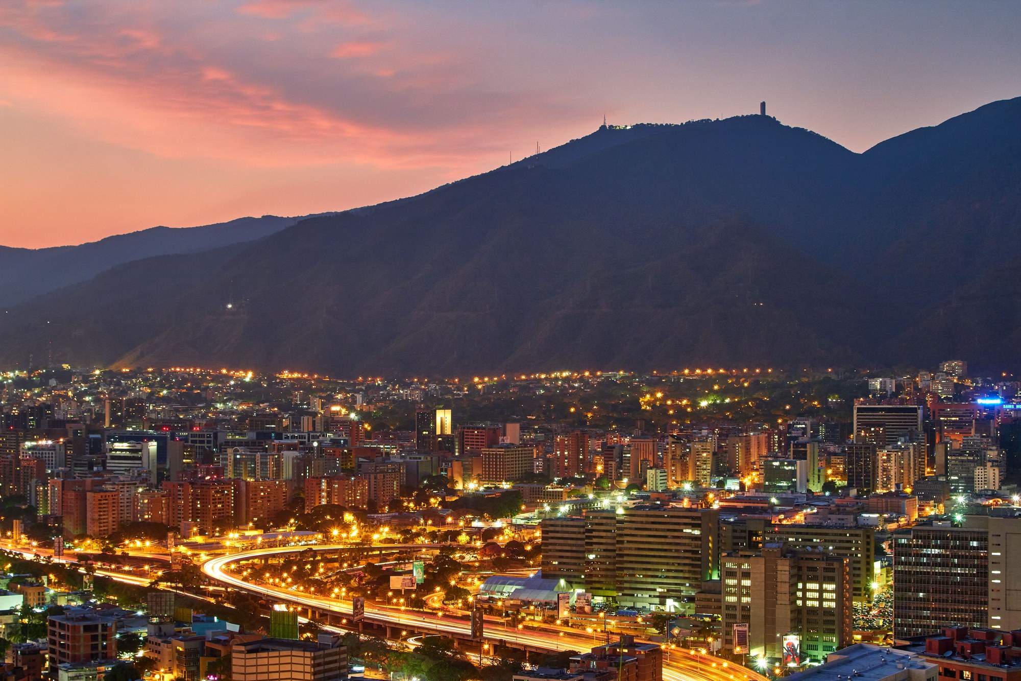 Cityscape of Caracas at dusk with glowing urban lights against dark mountain silhouettes