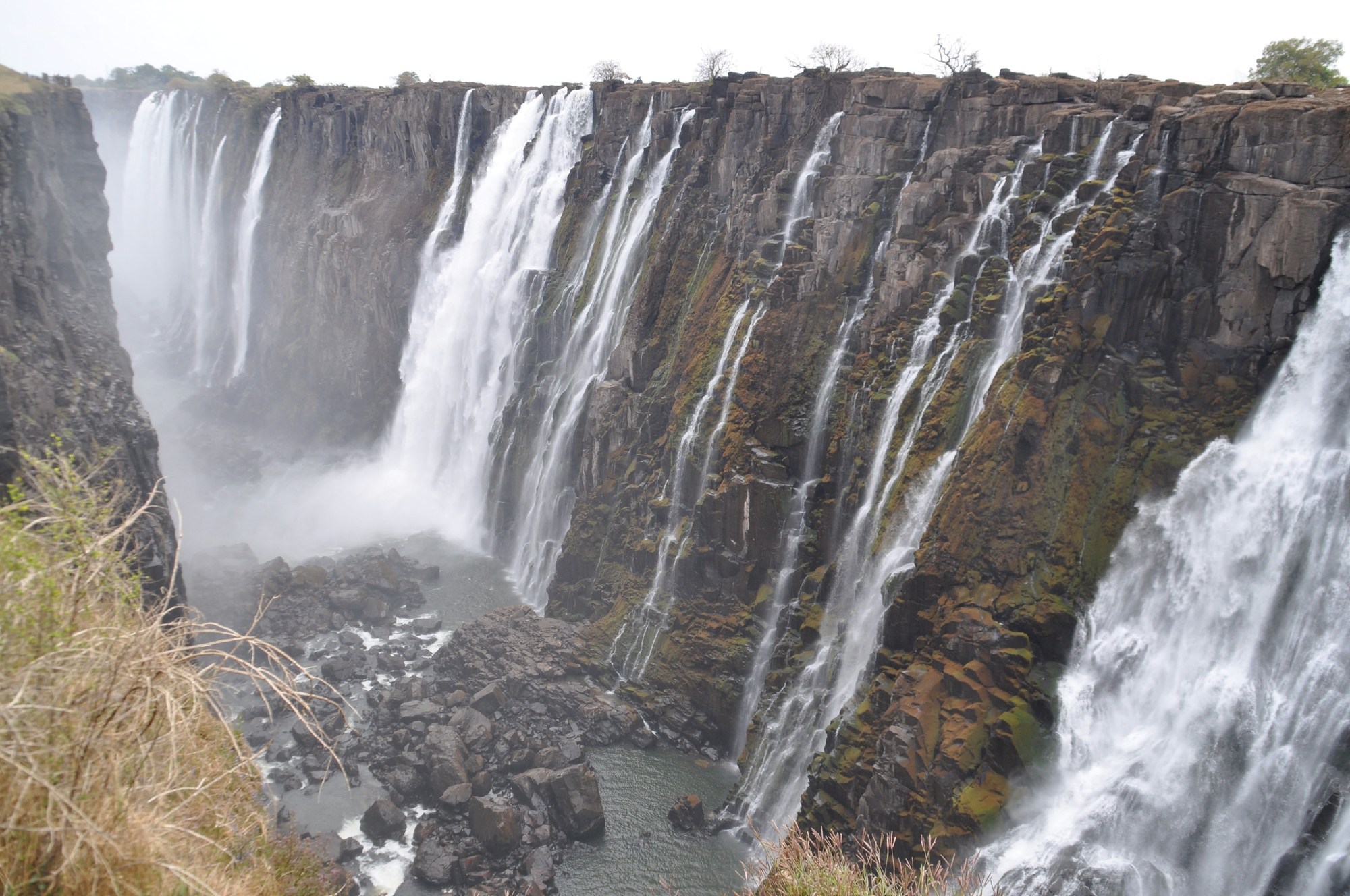 Wide shot of cascading waterfall curtains dropping over basalt cliffs into deep gorge