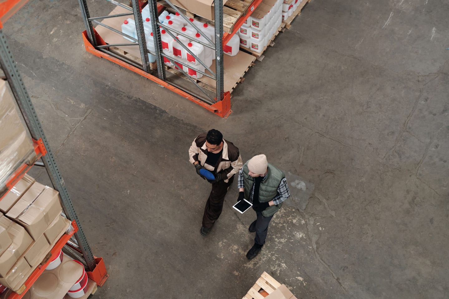 Two workers discussing inventory in a warehouse, using a digital tablet for coordination