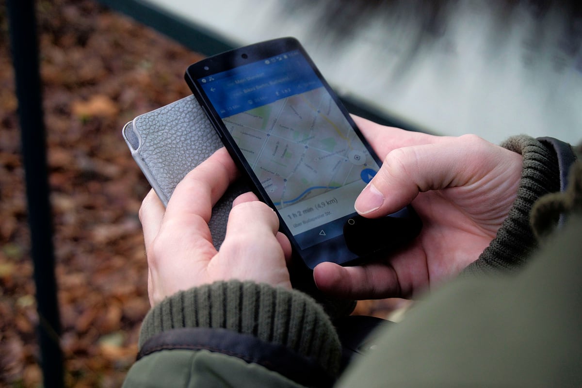 A person holding a smartphone displaying an active map navigation route while traveling