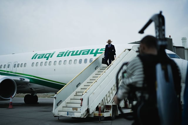 Man boarding Iraqi Airways plane via steps at an airport. Traveler scene.