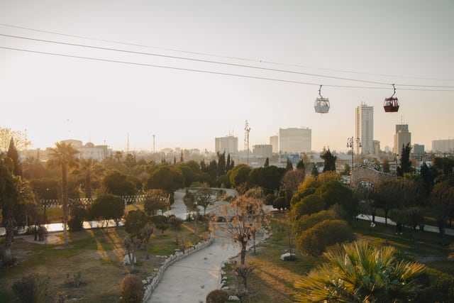 Stunning aerial view of a park in Erbil, Iraq with cable cars and the city skyline at sunset.