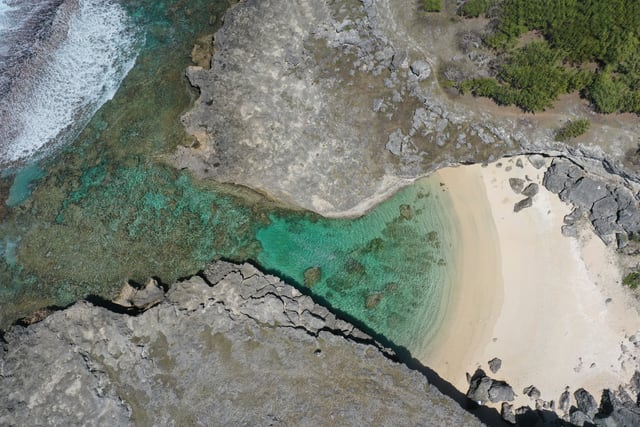 Stunning aerial shot of a secluded beach cove in Rodrigues, Mauritius, showcasing clear turquoise waters and rugged coastline.