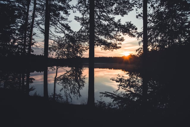 Peaceful sunset view with tree silhouettes reflecting on a lake in Dalarna County, Sweden.