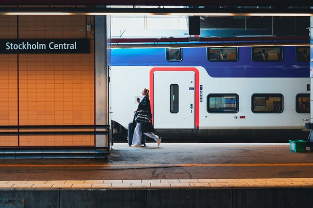 Woman walking with luggage at Stockholm Central Station's platform, beside a train.