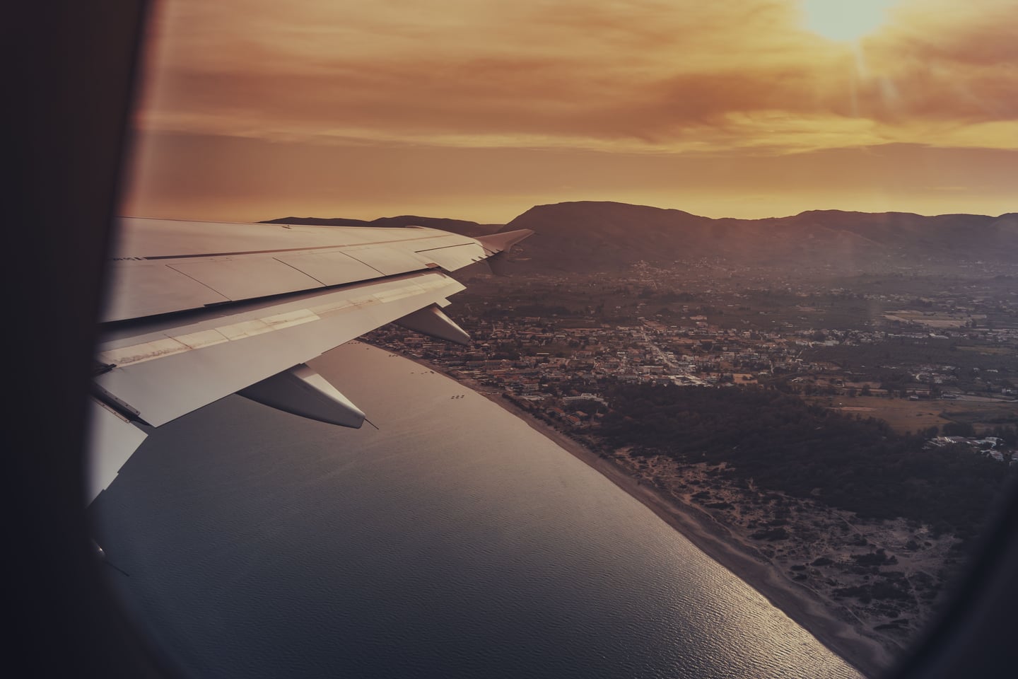 An airplane window view looking over a scenic coastline and mountains during golden hour.