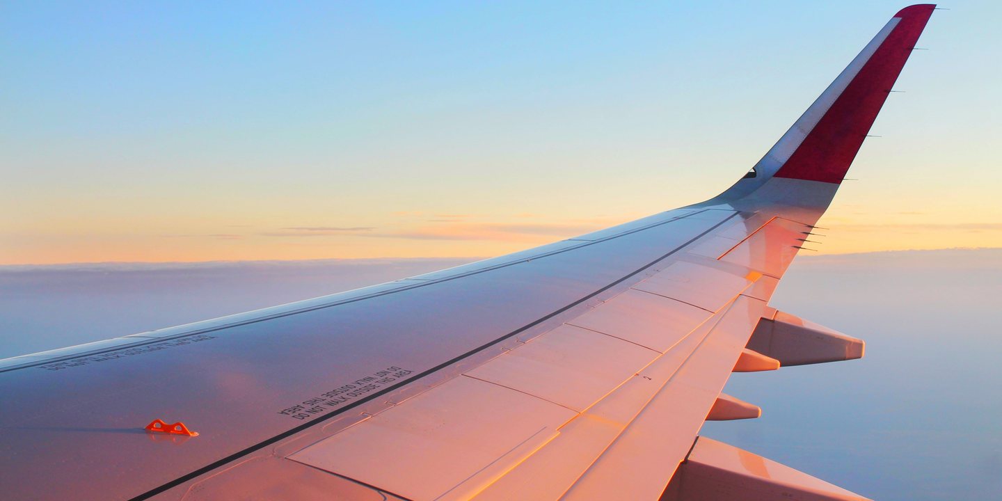 Airplane wing flying above golden clouds at sunset