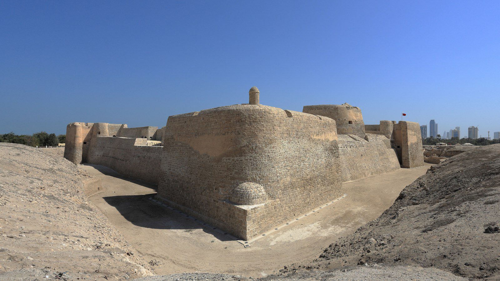 Massive excavated limestone ramparts and bastions of Qal'at al-Bahrain under clear blue skies