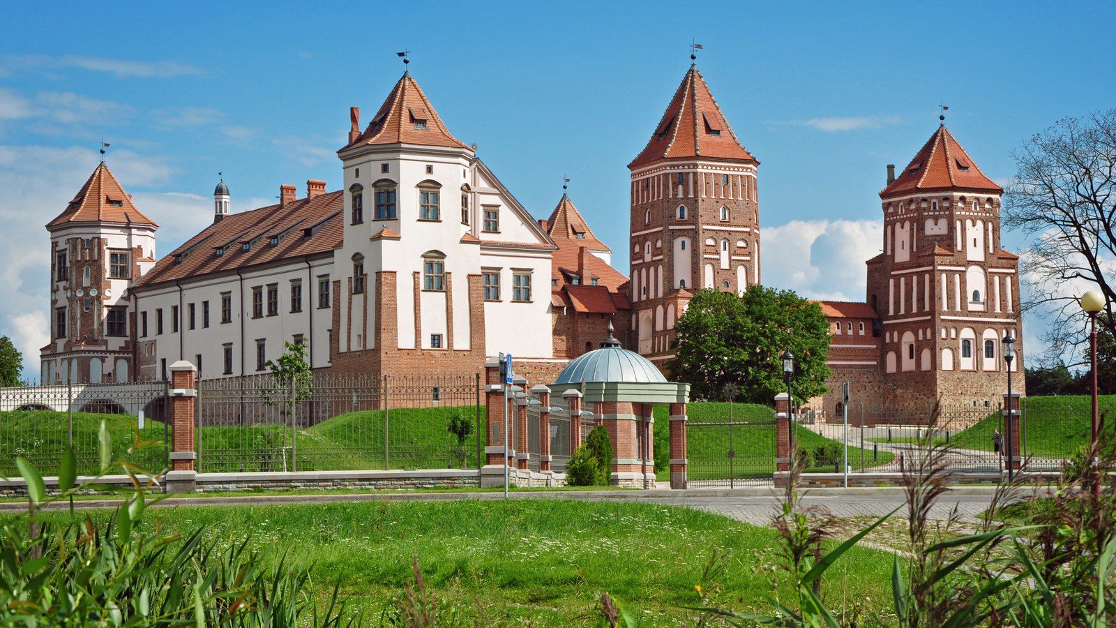 Panoramic landscape view of the red brick towers and fortifications of Mir Castle Complex reflected in the adjacent pond in Belarus