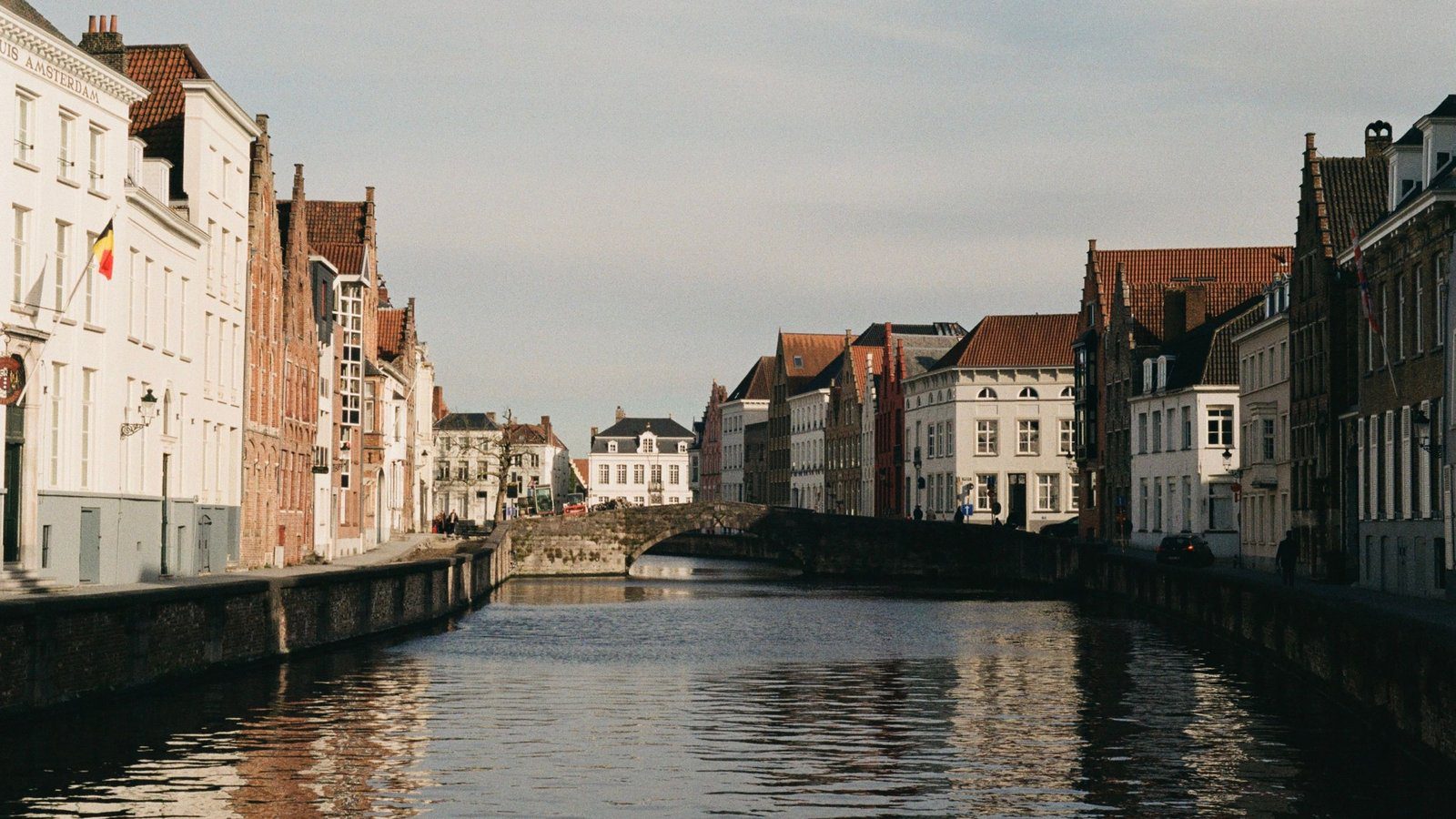 Scenic view of Bruges canal and historic Flemish buildings under clear sky.