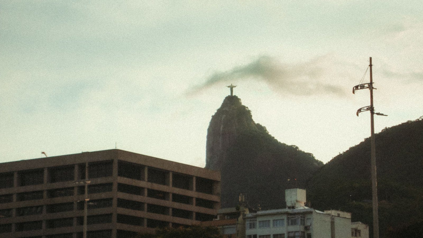 Christ the Redeemer statue on Corcovado Mountain with Rio de Janeiro cityscape under a cloudy sky.