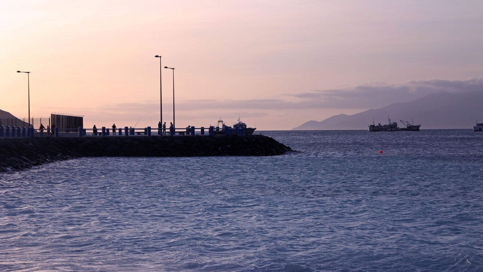Vessels moored in the coastal harbor against arid volcanic mountain ridges in Cape Verde