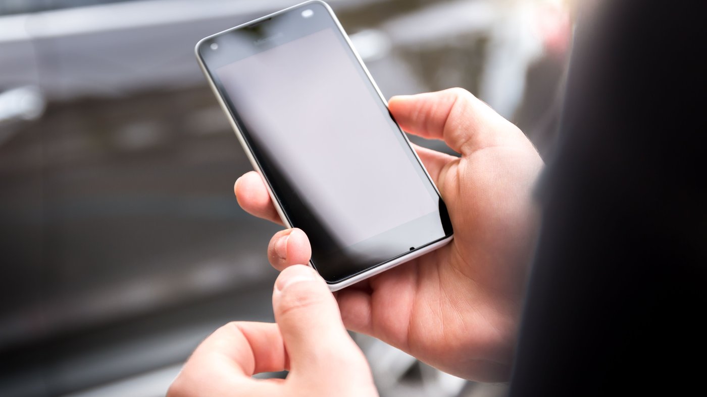 Hands holding a smartphone with a blank screen outdoors
