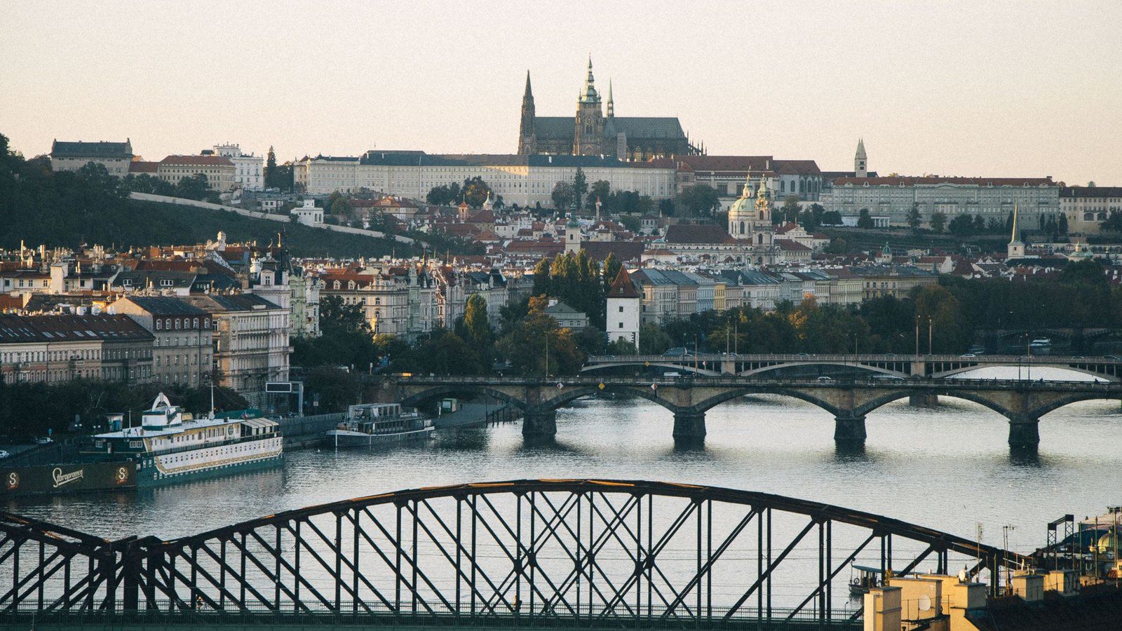 Scenic view of Prague's historic skyline, featuring the Vltava River and Prague Castle at sunset.