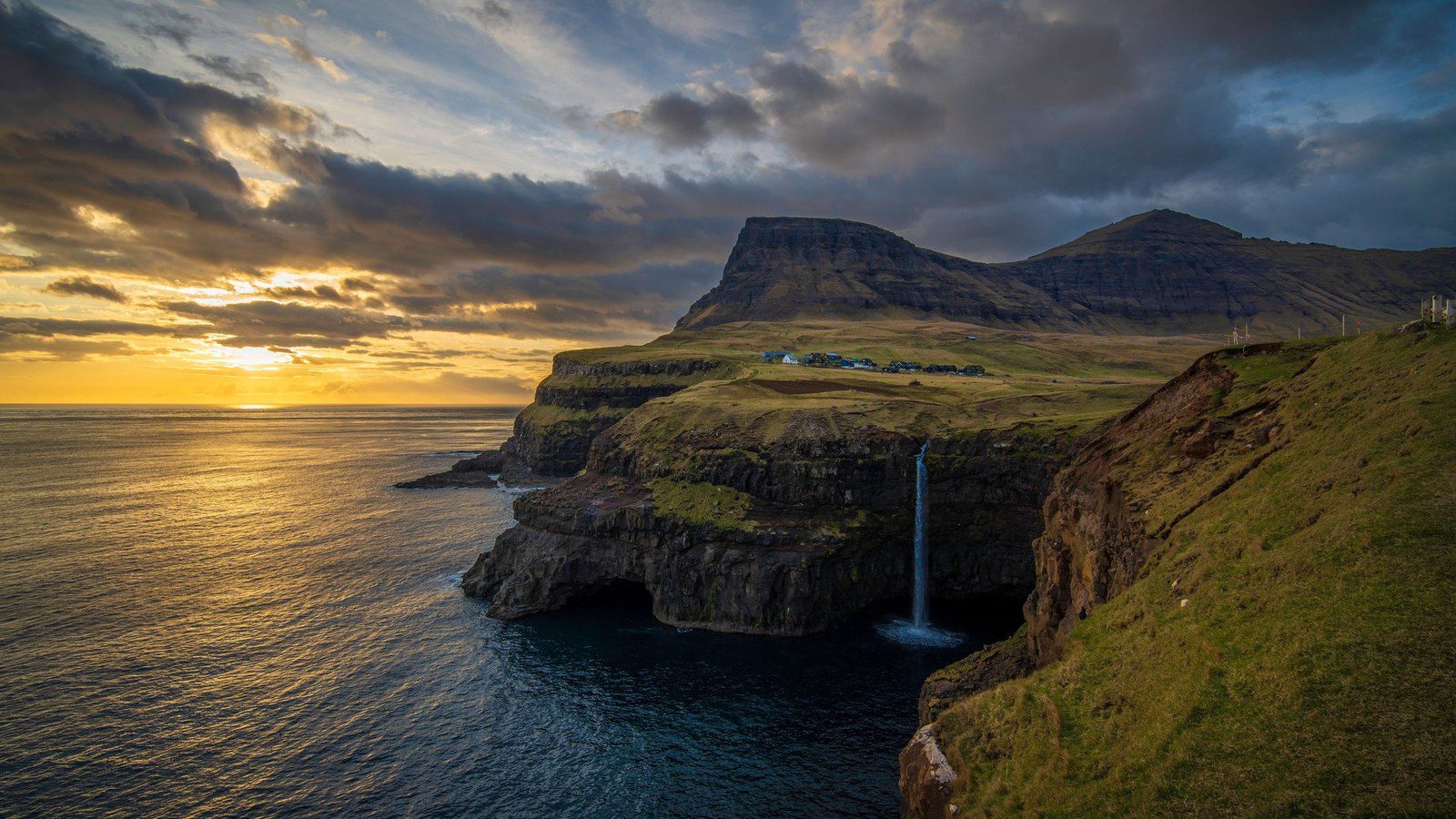 Múlafossur waterfall cascading over sheer basalt cliffs directly into the North Atlantic ocean at sunset near Gásadalur in the Faroe Islands