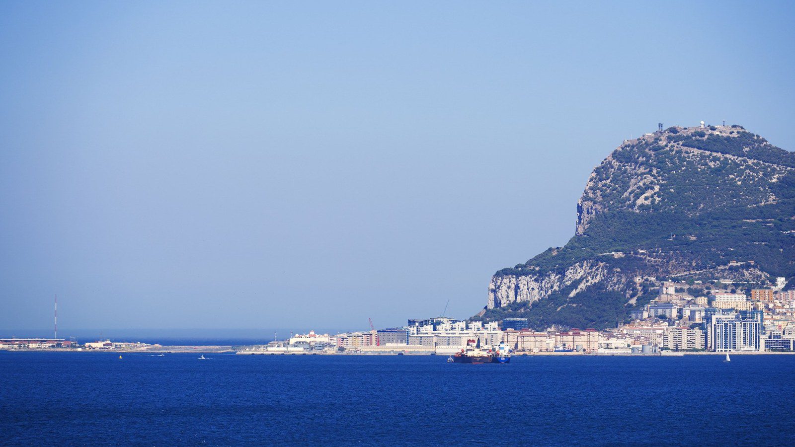 The monolithic limestone Rock of Gibraltar rising dramatically above the Mediterranean Sea under clear blue skies