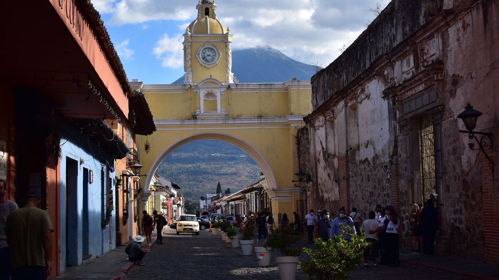 The iconic yellow Santa Catalina Arch framing the towering peak of Volcan de Agua along a cobblestone street in Antigua Guatemala