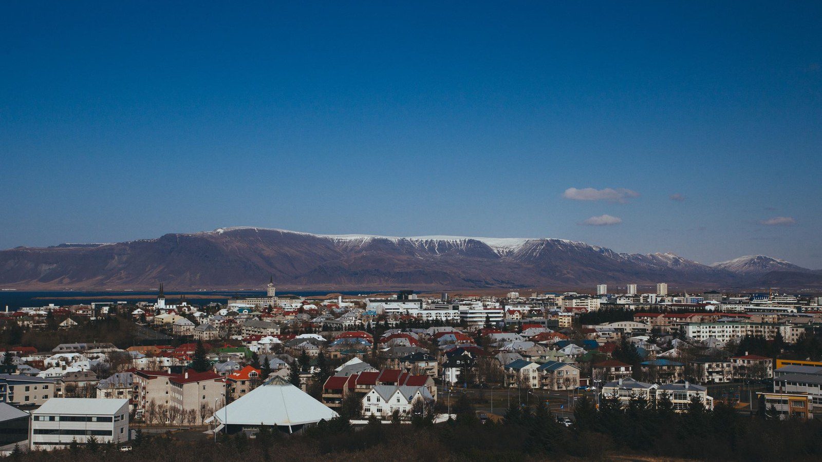 Breathtaking aerial view of Reykjavik cityscape, framed by majestic mountains under a clear blue sky.