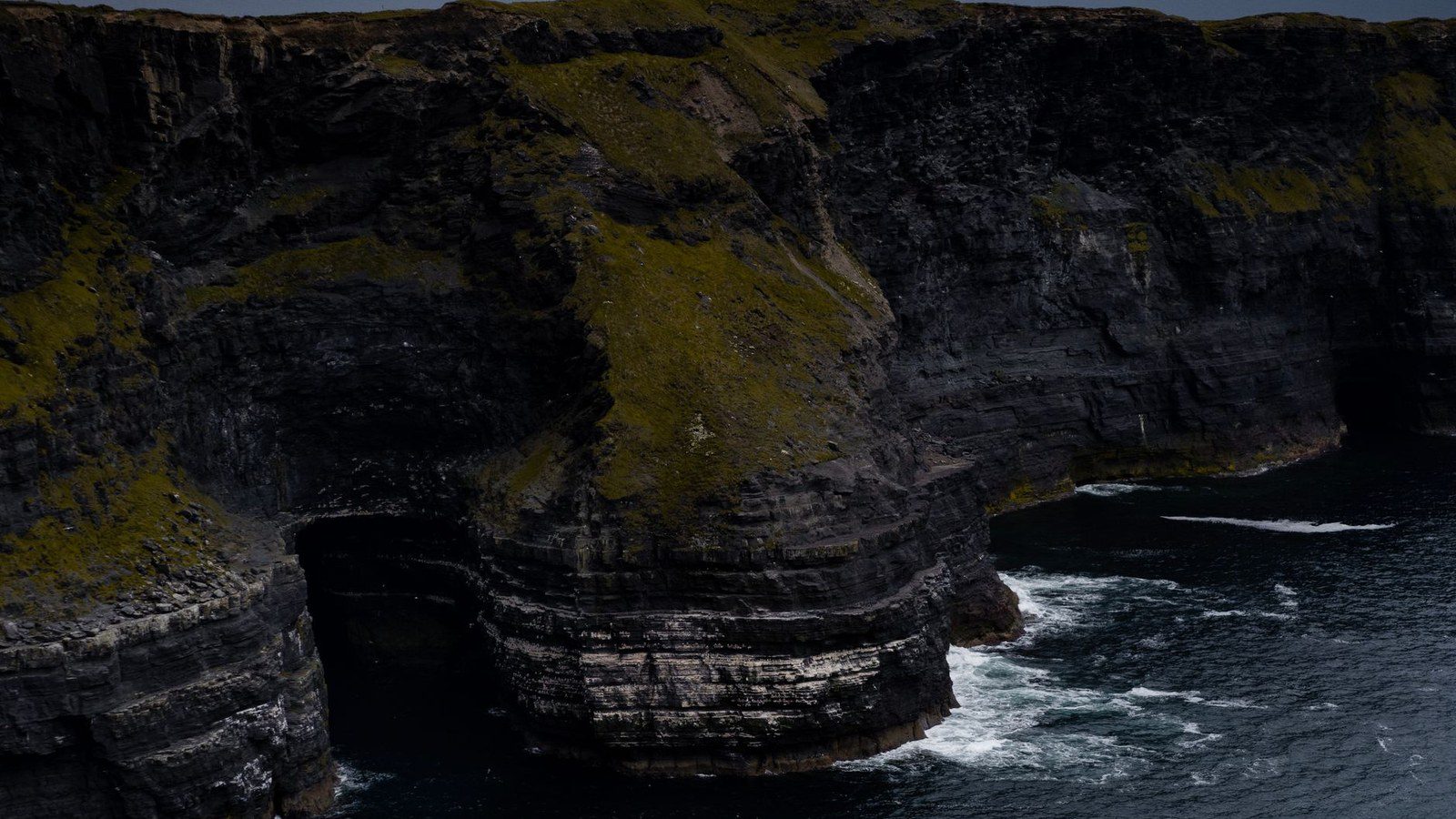 Stunning view of rugged cliffs with ocean waves crashing below on a gloomy day.