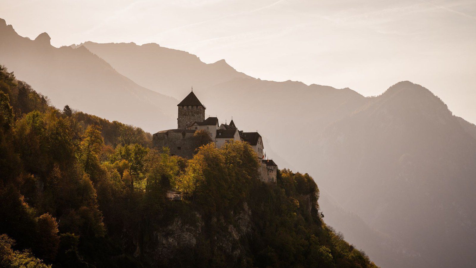 Panoramic autumn view of medieval Vaduz Castle perched on a forested rocky ridge overlooking the Rhine Valley in Liechtenstein