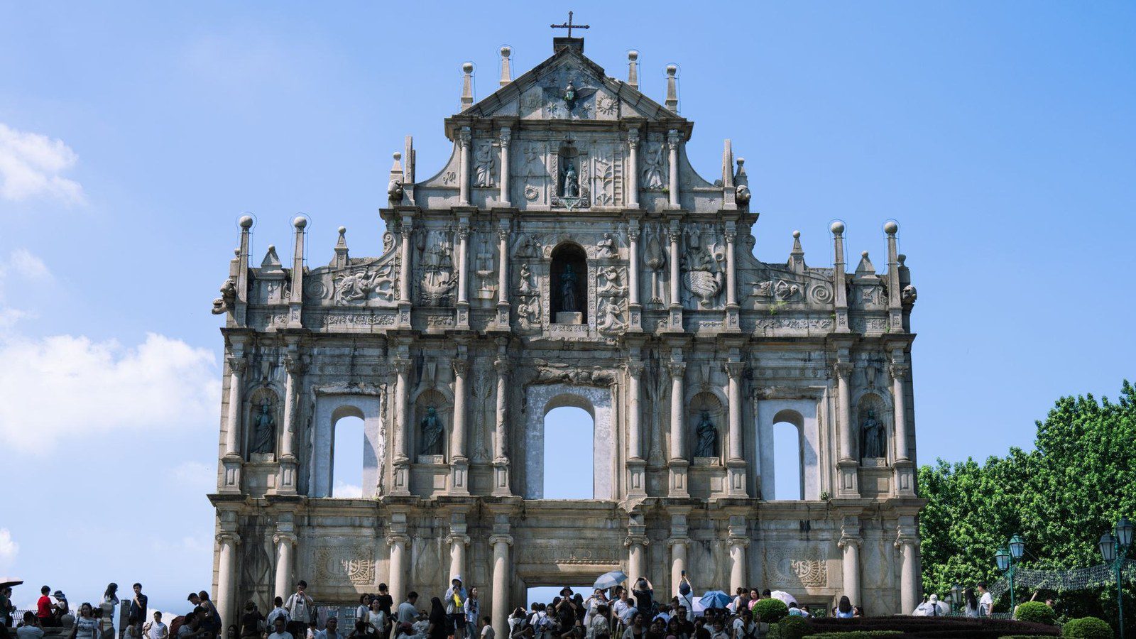 Iconic carved stone facade of the sixteenth-century Ruins of Saint Paul with visitors on the grand stone stairway under blue sky in Macao