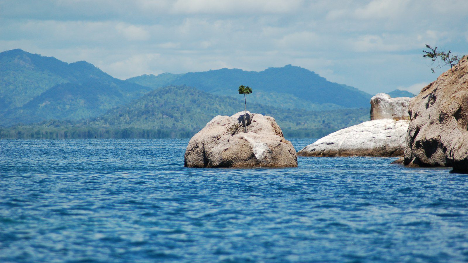 Golden sandy beach, wooden fishing boats, and calm turquoise waters of Lake Malawi bordered by green hills in Cape Maclear, Malawi