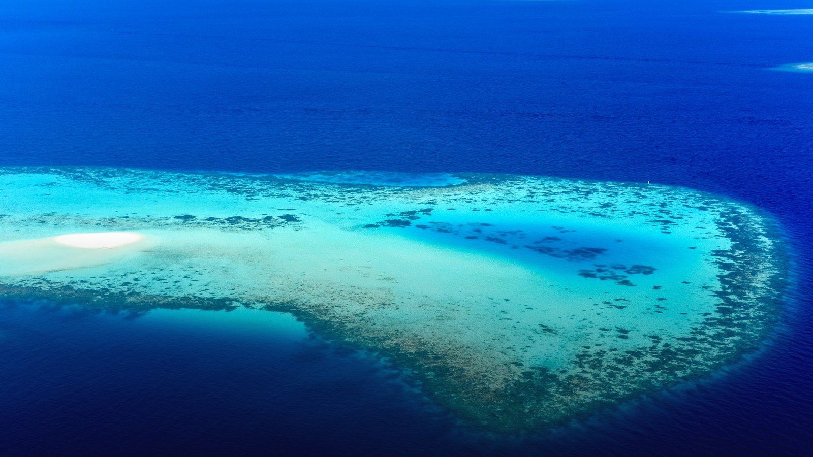 Aerial view of turquoise lagoon waters and circular coral reef barrier formations in the Indian Ocean