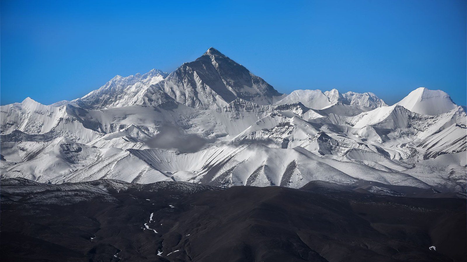Stunning view of Mount Everest surrounded by snowy peaks under a clear blue sky.