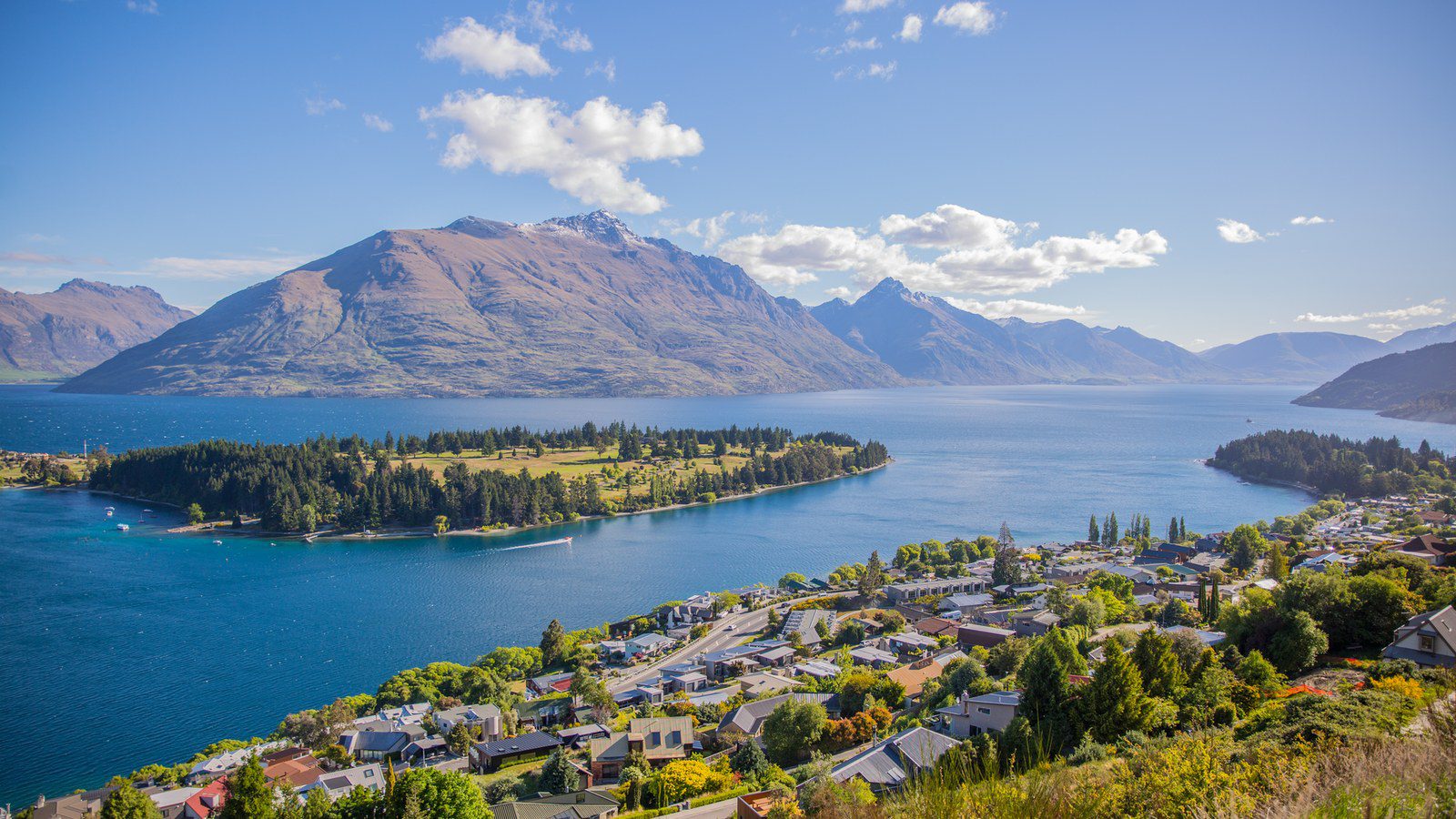 Breathtaking aerial view of Queenstown by Lake Wakatipu, surrounded by majestic mountains under clear skies.