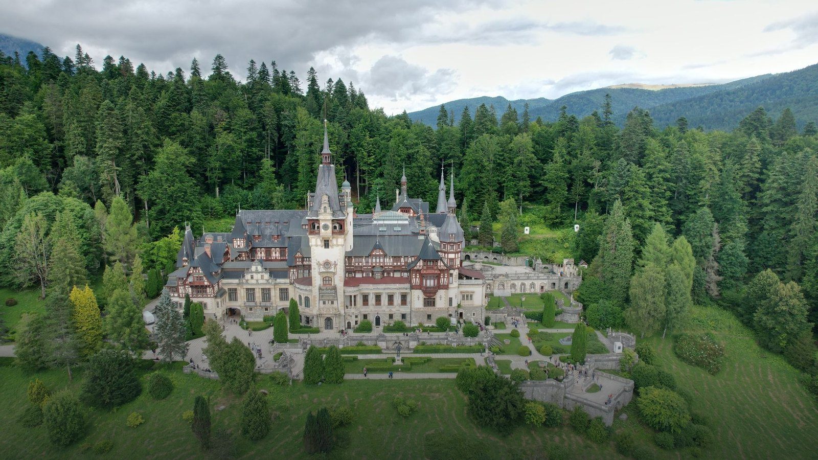 Neo-Renaissance timber-framed facade and stone towers of Peleș Castle surrounded by forested Carpathian hillsides in Sinaia