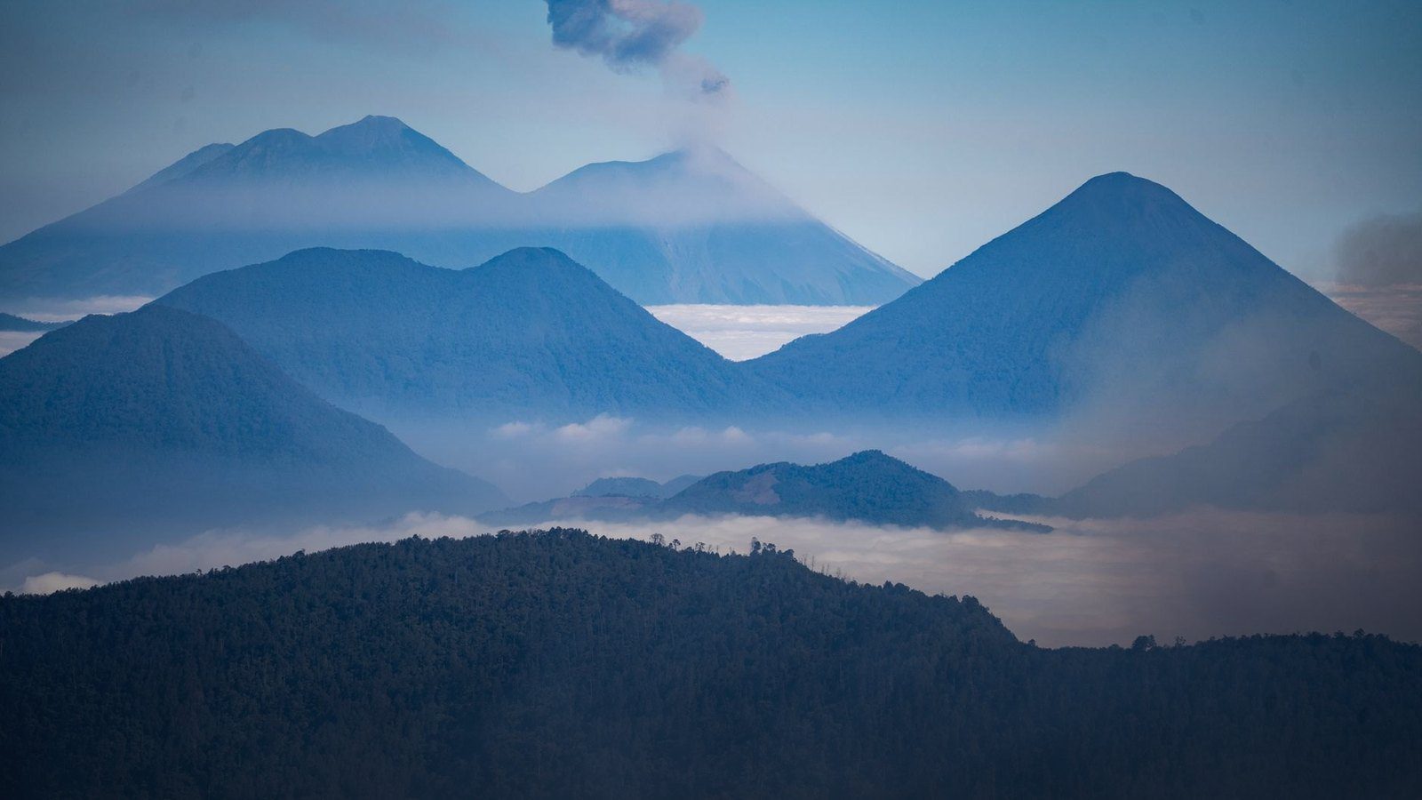 Volcanic mountain peaks covered in dense green rainforest enveloped in low-hanging mountain mist and cloud