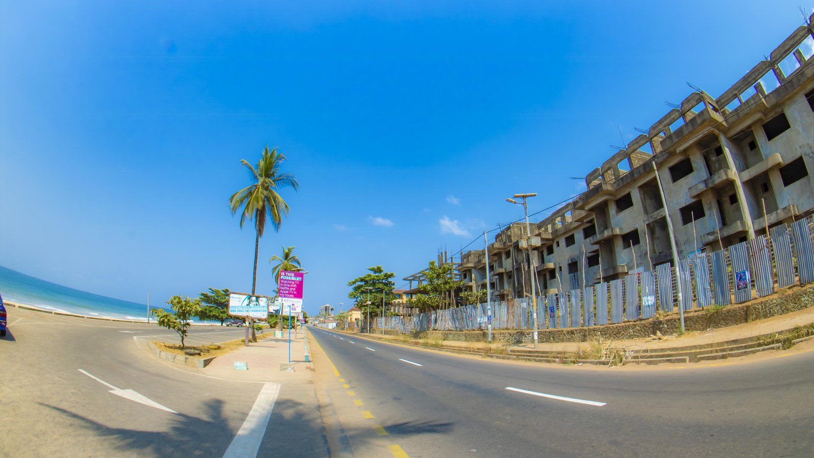 Paved coastal road and palm trees bordering golden Atlantic sands along Aberdeen beach in Freetown, Sierra Leone
