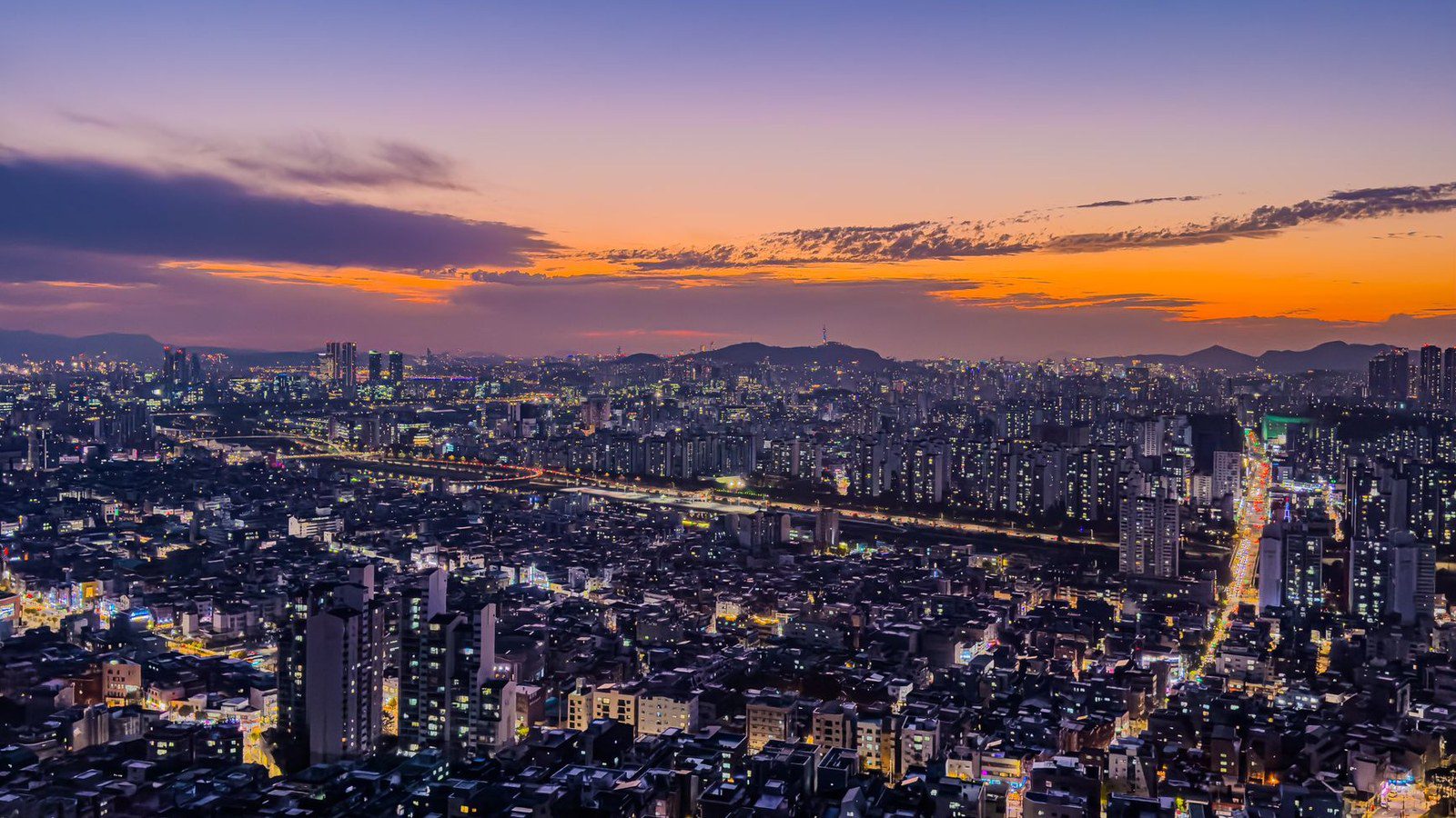 Breathtaking aerial view of Seoul at sunset, showcasing vibrant city lights and skyline.