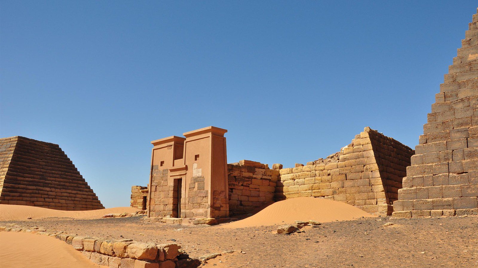 Steeply pitched sandstone Nubian pyramids of Meroë rising above golden desert sands in Sudan