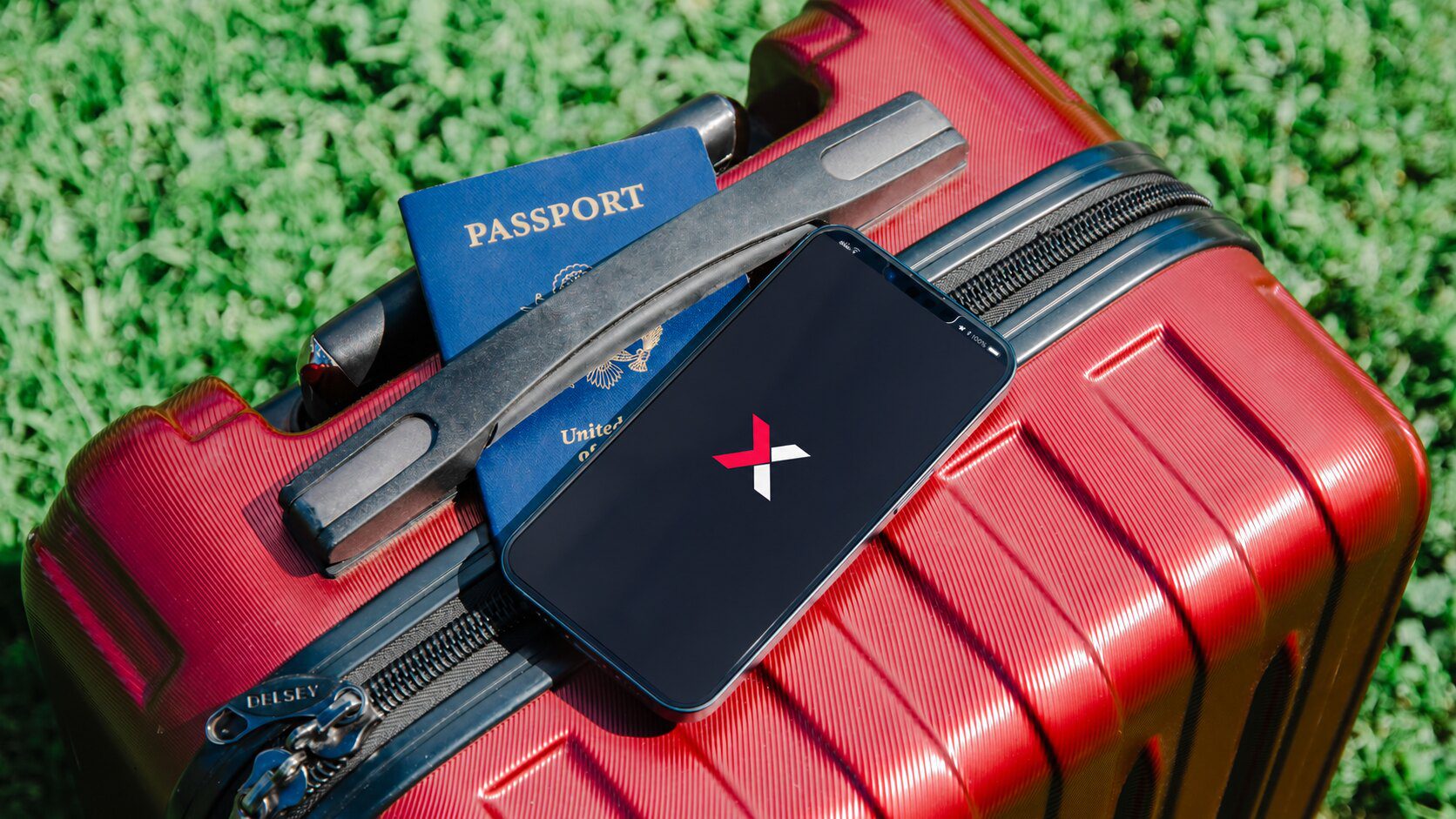 Smartphone showing the NXTL X on a red suitcase beside a passport, for a travel eSIM comparison