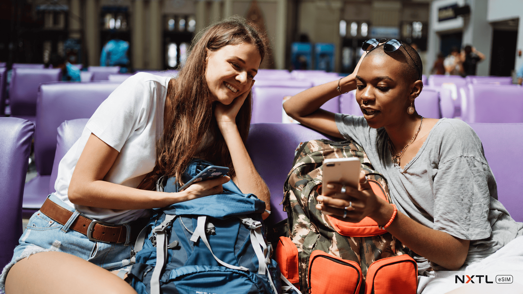 Two travelers with backpacks checking their phones in an airport waiting area